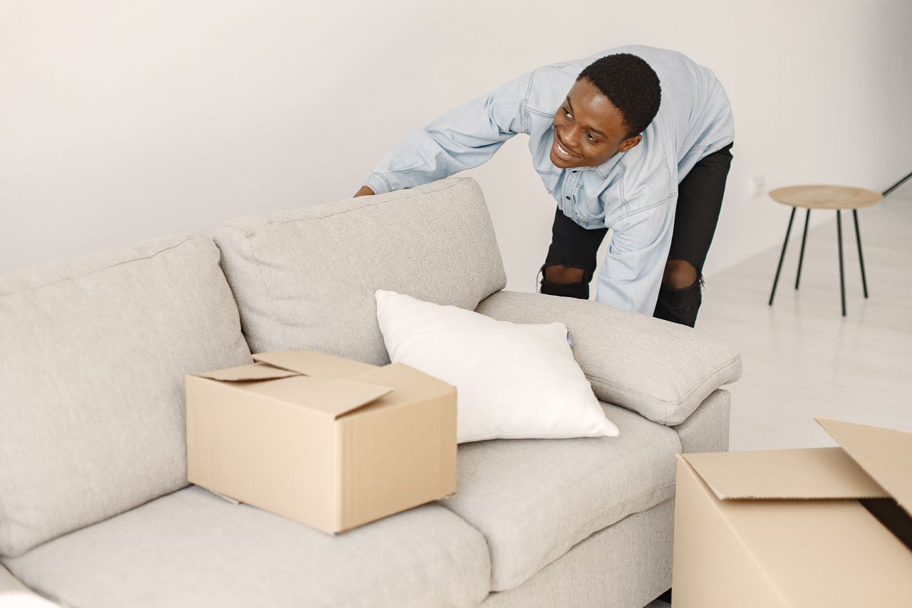 Young man smiling while arranging cardboard boxes in a modern living room.