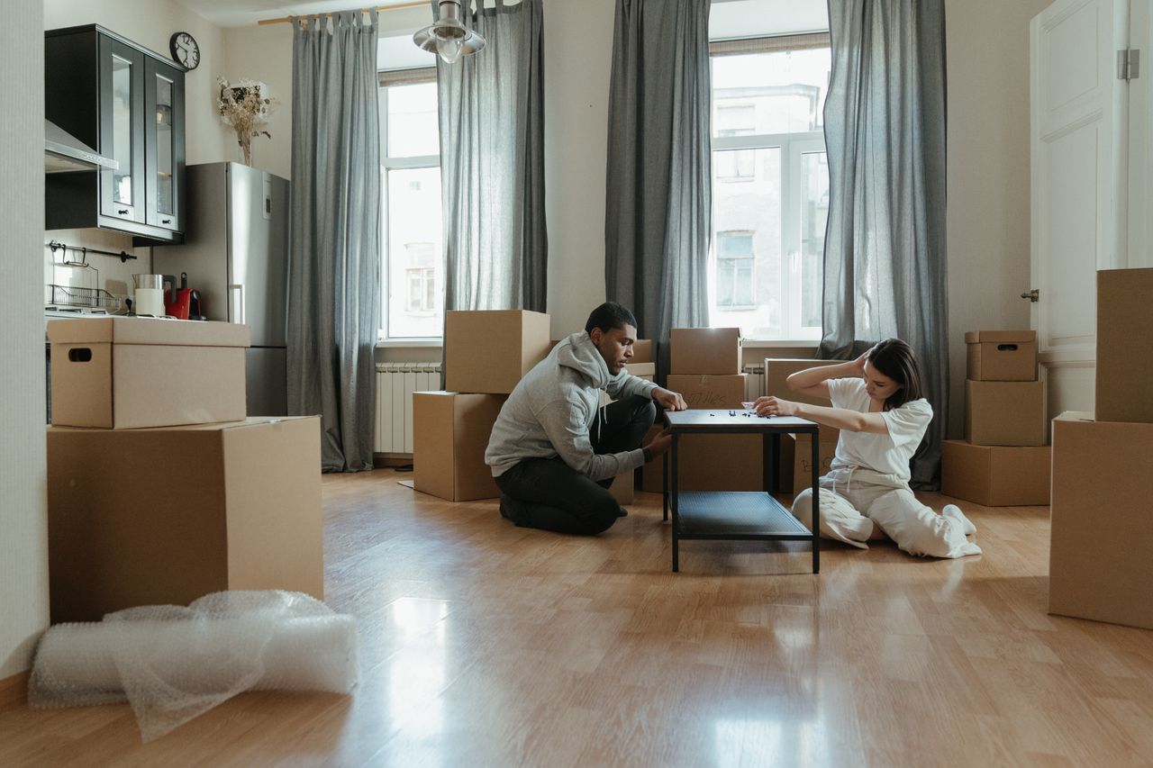 services-03 Young couple assembling furniture in their new apartment, surrounded by cardboard boxes.